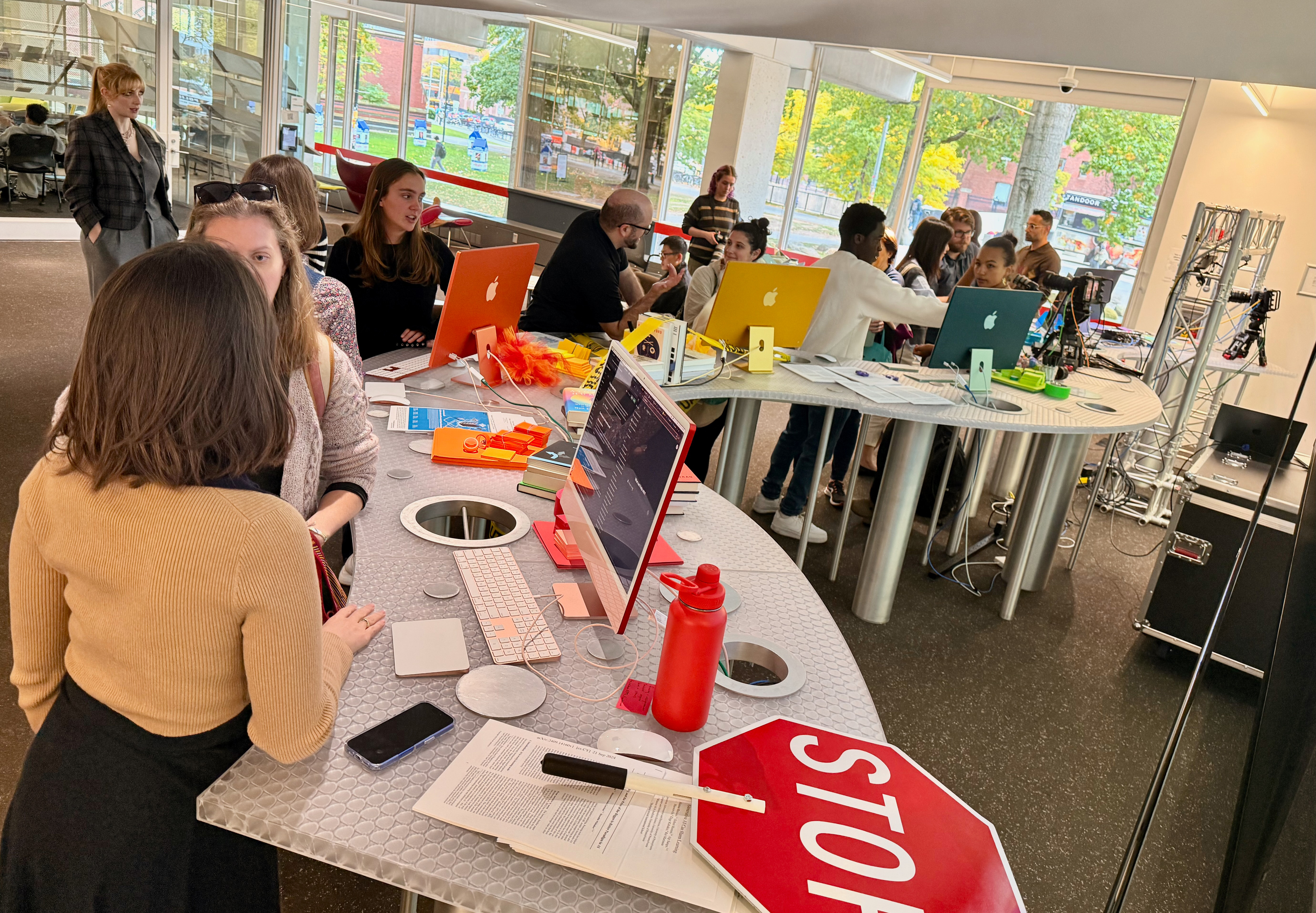 people gathered around a curved table with the rainbow of iMacs, discussing AI
